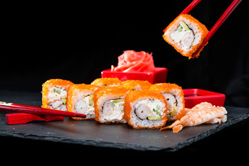 traditional Japanese cuisine. Process of eating sushi rolls with cream cheese, rice, caviar, avocado, cucumber and shrimp on dark background, selective focus