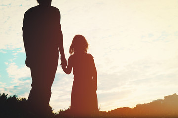 silhouette of father and daughter holding hands at sunset