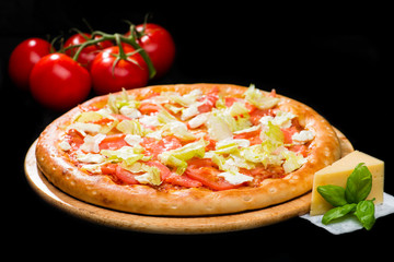 selective focus on appetizing Italian pizza cheese, sliced tomatoes and cabbage leaves on round wooden board on dark background, near tomatoes and cheese