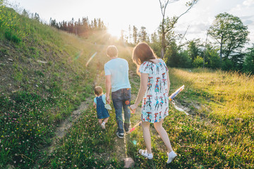 Fototapeta premium mother and father holding daughter hands and walking by mountains