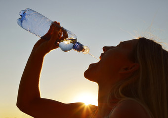 Silhouette of a woman drinking water from bottle at sunset.