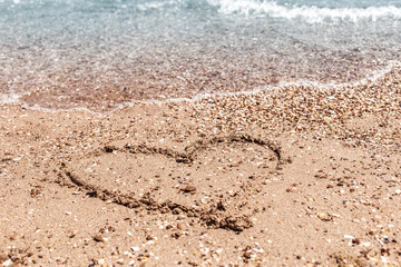Drawing of a heart on the sand on the beach and wave with foam. Sea travel and holiday. Selective focus