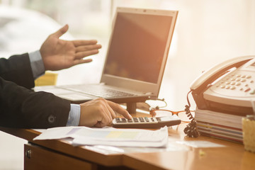 A businessman analyzing investment charts at his workplace and using his laptop and touch calculator.