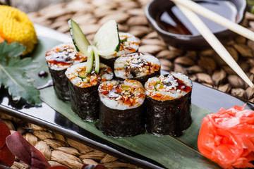 Sushi Roll - Maki Sushi with Smoked Eel, cucumber, avocado and sesame on black stone on bamboo mat decorated with flowers. Japanese cuisine