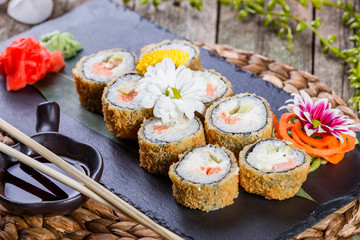 Hot fried Sushi Roll - Maki Sushi with salmon, cucumber, avocado and cream cheese on black stone on bamboo mat decorated with flowers. Japanese cuisine