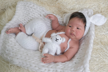 cute asian boy newborn portrait  with white doll one month lie down  on white background fur .