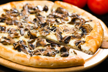 selective focus on sliced piece of appetizing Italian cheese pizza with marinated mushrooms on the foreground, and whole pizza on the background, close-up