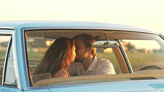 Young cute lovers hugging and kissing in car against sunset