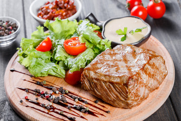 Grilled steak pork with fresh vegetable salad, tomatoes and sauce on wooden cutting board