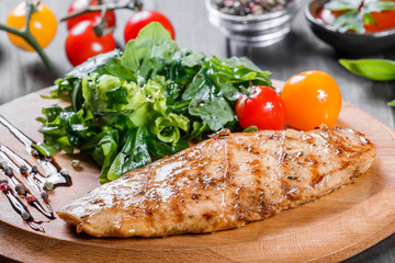 Grilled chicken fillet with fresh vegetable salad, tomatoes and sauce on wooden cutting board