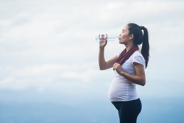 Active healthy pregnant woman drinking a bottle of water on top of mountain.