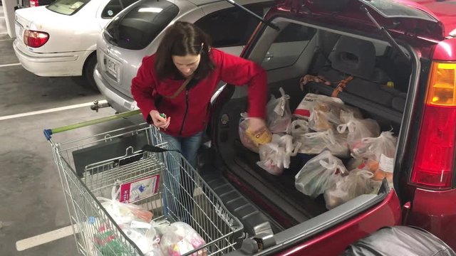 Young adult woman (age 30 -35) loading shopping bags into a car in a parking lot after shopping activity in the supermarket. Consumption concept. Real people. Copy space