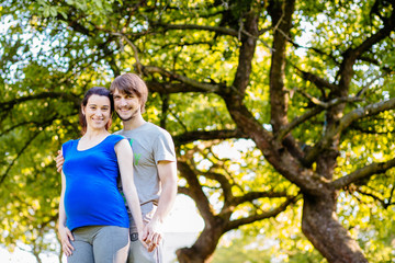 Fototapeta premium Pregnant couple over beautiful green tree background. Parenthood, sport and healthy life concept.