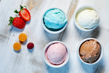 Selection of gourmet flavours of Italian ice cream in vibrant colors served in individual porcelain cups on an old rustic wooden table in an ice cream parlor, angle view jpg