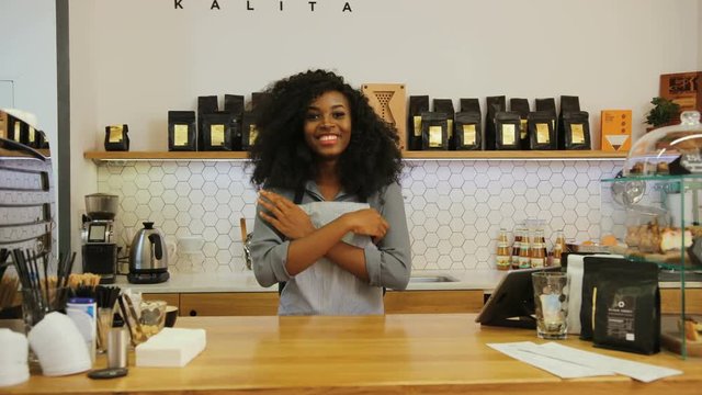 Portrait of female african barista crossing hands and smiling on the camera in the coffee cafe.