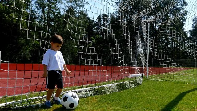 Tracking camera of a little 3 years old boy scoring a goal in a football field