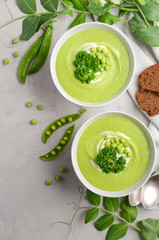 Green pea soup in bowls on grey concrete or stone background, top view, close-up