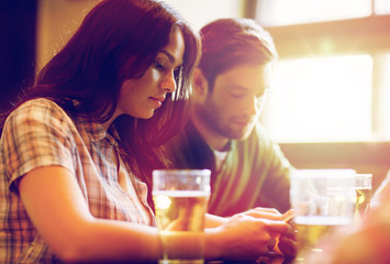 friends with smartphones drinking beer and at pub