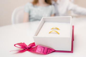 Golden wedding rings in a beautiful box packing in front of the hands of a young family