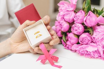 Wedding rings of gold in the hands of the newlyweds on the background of a wedding bouquet of generic flowers