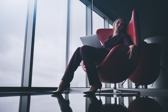 Tired And Relaxed Boss Woman With Laptop Is Sprawling In Bent Red Armchair In Office Chill Out Area And Dreamy Looking Up, With Copy Space Place For Logo, Your Text Or Other Advertising