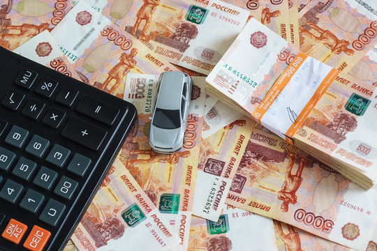 The concept of buying a car: model cars, a calculator and a stack of Russian rubles in the banking package lying on the background of scattered banknotes