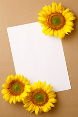 Fototapeta premium Sunflowers on a brown background with a blank paper. Copy space. Top view. Summer greeting card