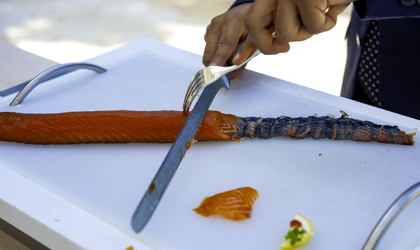Male hands slicing salmon fillet on the white cutting board, close-up.