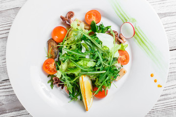 Seafood salad with mussels, squids, octopus, arugula, lettuce and cherry tomatoes on wooden background close up. Mediterranean food