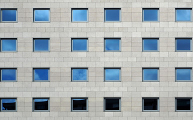 Gray stone modern facade of a building with windows reflecting the sky