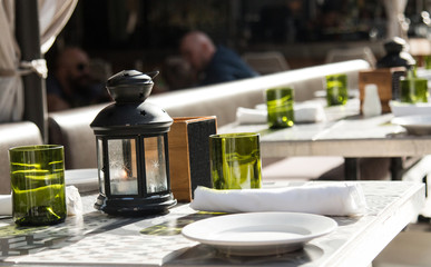Summer day restaurant setting decor with white plates, green glasses and black lanterns