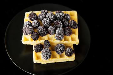 Belgian wafers with frozen blackberries on a black background, close-up.