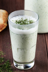 Ayran with fresh herbs in a glass, on dark wooden background with tortilla and pita bread. Traditional Turkish yoghurt drink.
