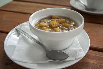 White bowl of a garlic soup with cheese, ham and bread croutons. Traditional Czech and Slovak dish on the table with spoon.