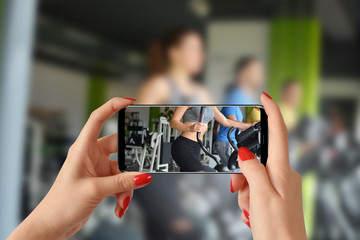 A woman shoots video with phone of group people while they train at a gym