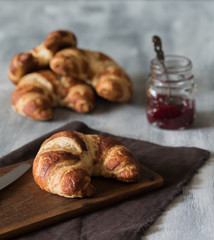 Croissant auf dunklem Holzbrett mit Erdbeermarmelade zum Frühstück auf hellem Untergrun