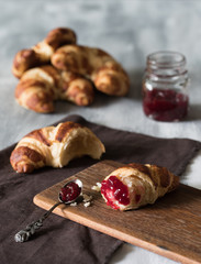 Croissant auf dunklem Holzbrett mit Erdbeermarmelade zum Frühstück auf hellem Untergrun