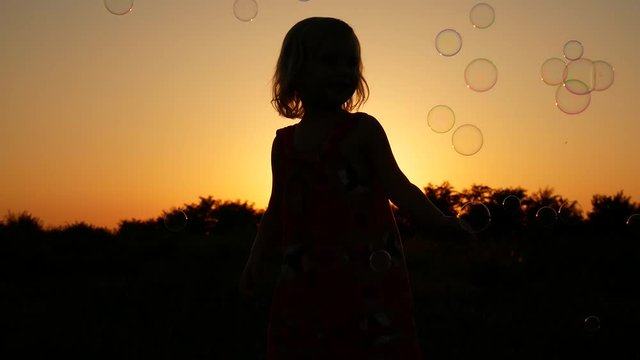 The child is played with soap bubbles. Video in slow motion on a sunset background.