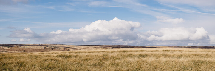 Blue sky and white clouds above sunlit moorland. Derbyshire, UK.