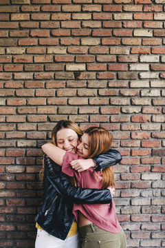 Happy best friends embracing in front of a brick wall.