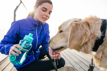 Runner woman gives water to her dog after workout.
