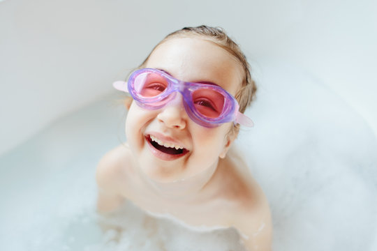 Cute young girl with swim goggles laughing in a bathtub
