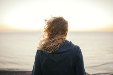 An anonymous blond woman standing in the wind looking at the sea or ocean