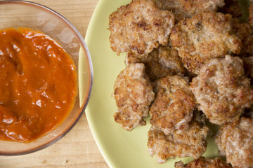 Mini pork patties, meatballs with bread, tomato sauce and fork on wood