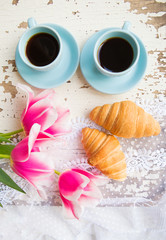 nice cup of coffee, croissants and pink tulips on old white table.