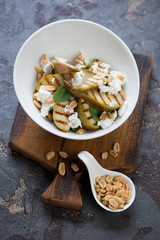 Salad with grilled pears, feta cheese, fresh spinach and nuts served in a white bowl on a brown stone background, studio shot