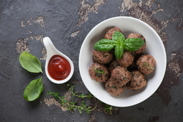 White bowl with baked meatballs and sauce on a brown stone background, view from above