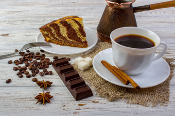 A cup of coffee on sacking with tasty chocolate cake on a plate. Cinnamon sticks, sugar, coffee...