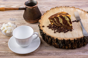 A chocolate cake on wooden stump with a coffee cup,fork, coffee beans and bowl with sugar cubes on a bright wooden background