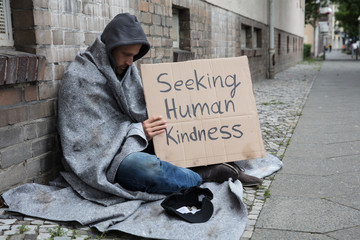 Beggar Showing Seeking Human Kindness Sign On Cardboard